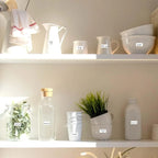 Étagère claire garnie de pots et de carafes portant chacun une petite étiquette blanche imprimée