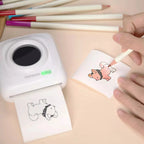 Imprimante blanche PAPERANG imprimant un dessin de chien, main coloriant l'impression au crayon, crayons de couleur autour