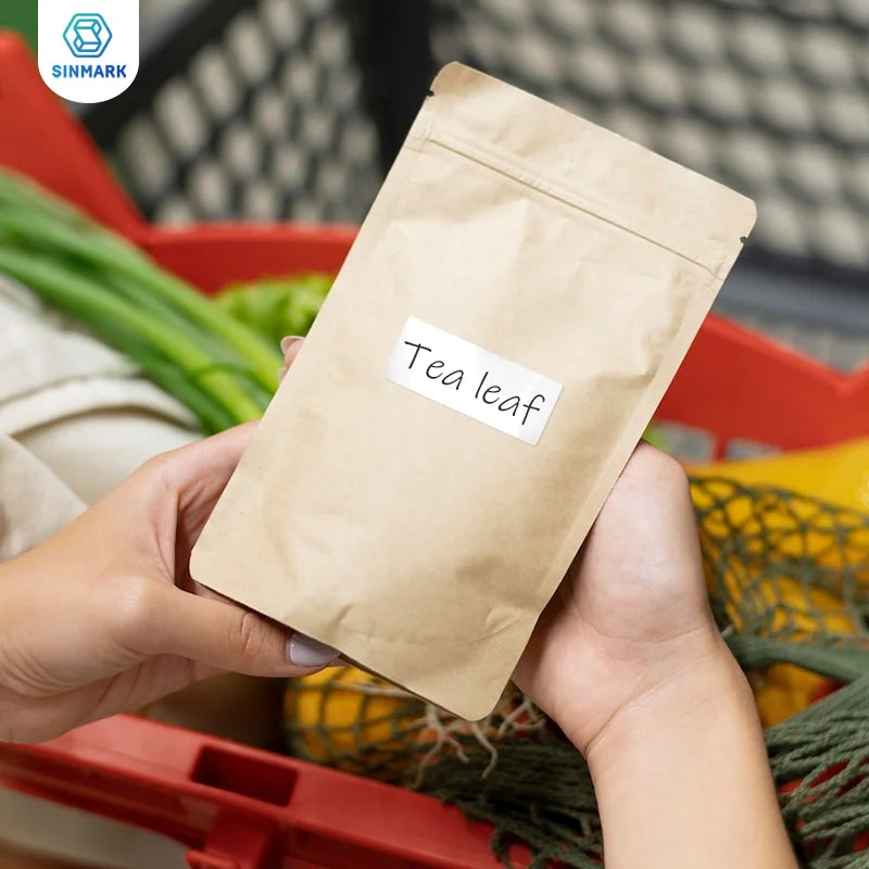 Mains tenant un sachet kraft portant une étiquette manuscrite Tea leaf, devant un cageot de légumes