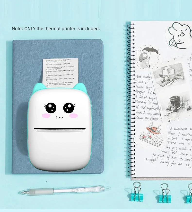 Imprimante chat menthe sur un carnet bleu, à côté d'un carnet à spirale rempli de textes et croquis collés