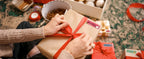 Mains nouant un ruban rouge sur un cadeau kraft portant une étiquette Merry Christmas, paquets autour