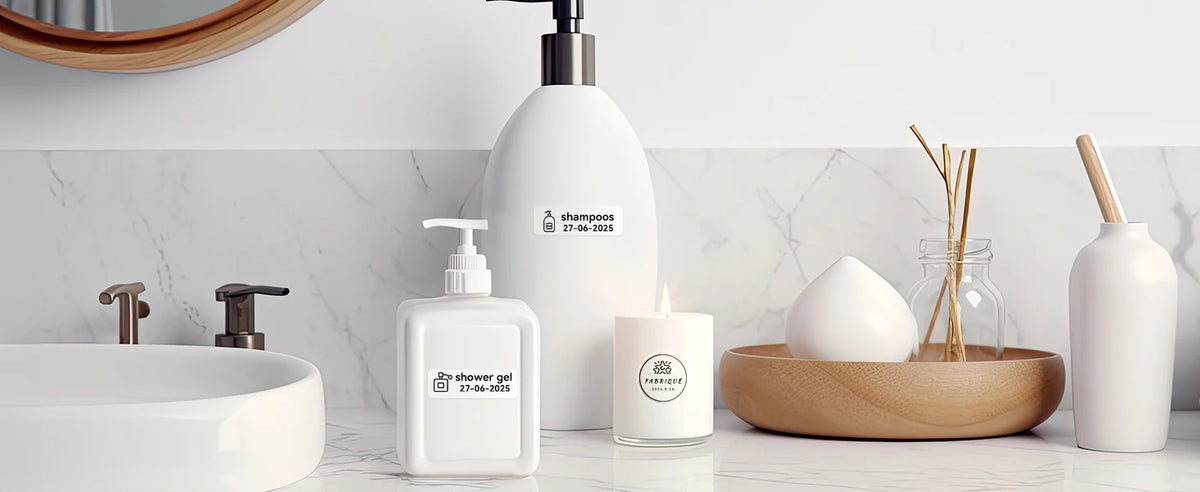 Salle de bains avec flacons étiquetés shampooing et gel douche datés, bougie et diffuseur sur le marbre
