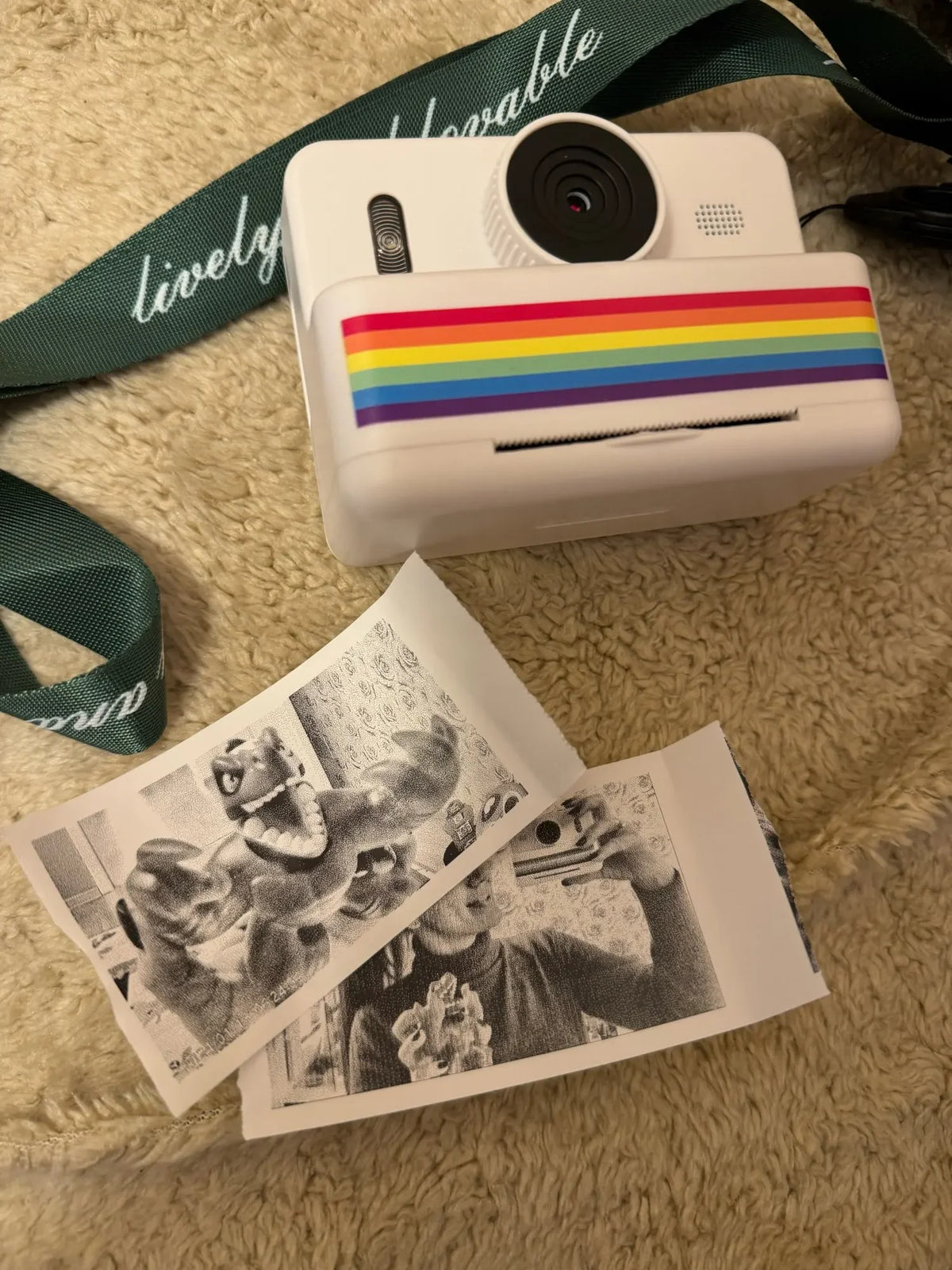 Appareil blanc à dragonne verte posé sur un tapis moelleux, près de trois photos imprimées en noir et blanc