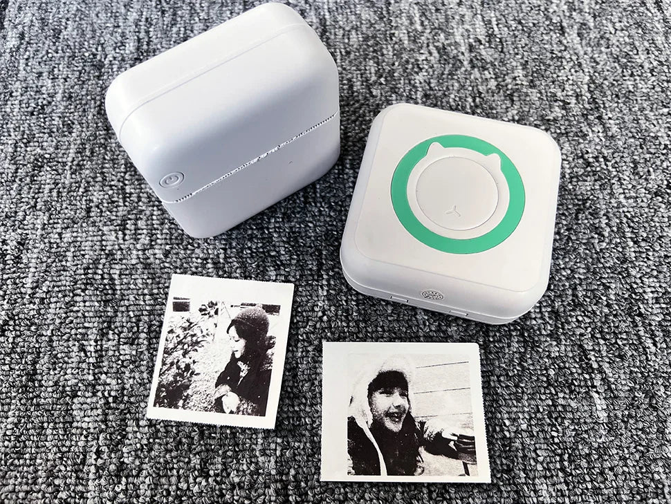 Mini imprimante blanche fermée et modèle à anneau vert, entourés de photos noir et blanc imprimées