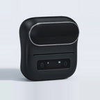 Imprimante d'étiquettes noire mate vue de trois quarts sur fond bleuté, écran vierge et voyant de batterie allumé
