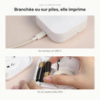 Deux alimentations : câble USB-C branché sur l'imprimante, et compartiment à quatre piles AAA ouvert